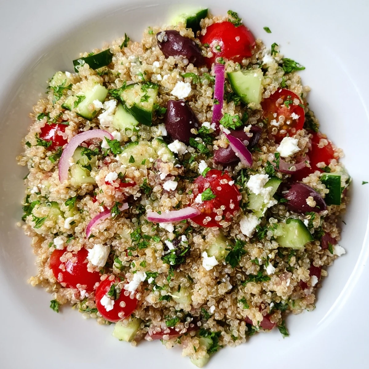 A spoon scoops into chilled Mediterranean Quinoa Salad with Cucumber and Feta, revealing colorful cherry tomatoes, Kalamata olives, and crumbled feta cheese.