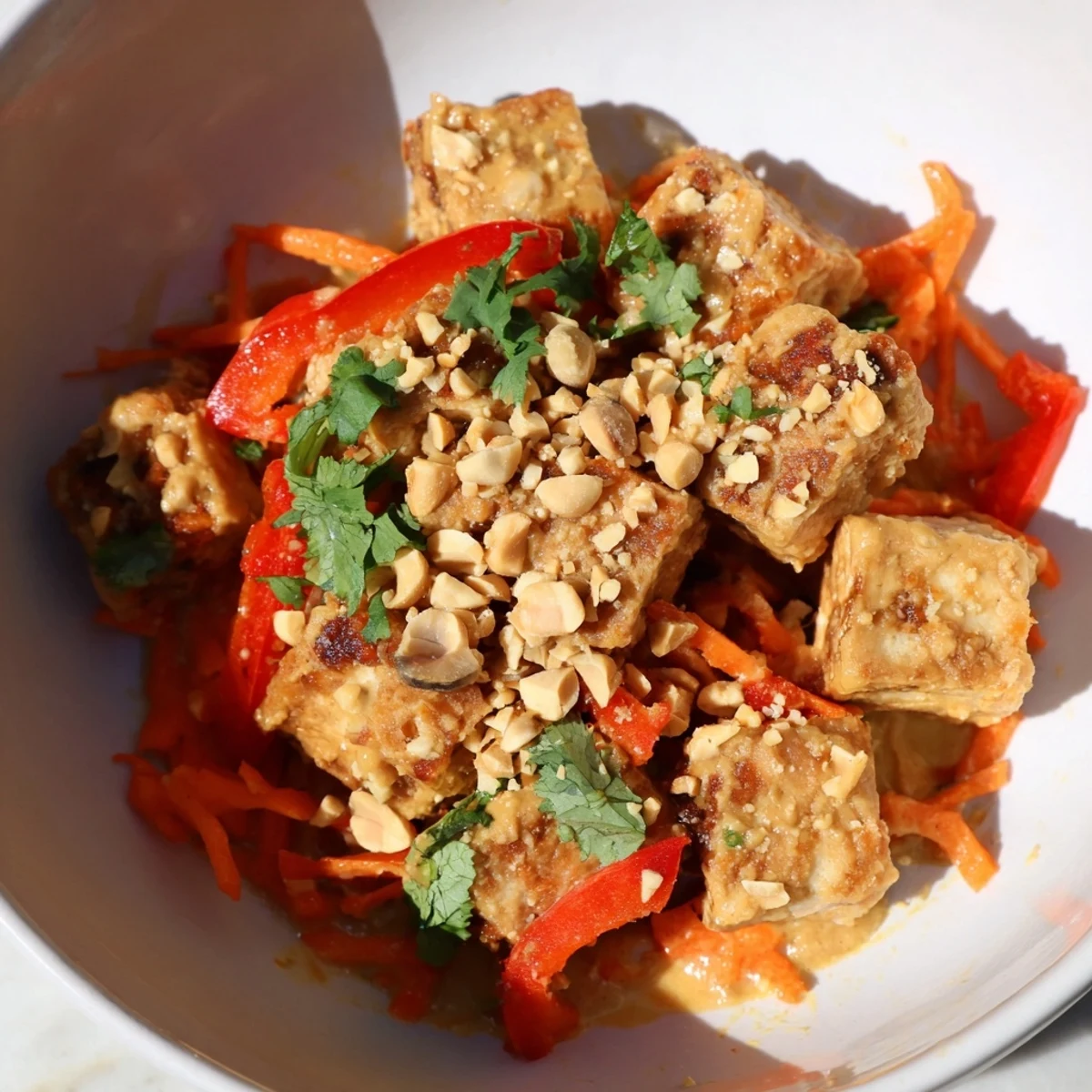 Bright stir-fry vegetables and crunchy peanuts garnish a plate of savory Crispy Tofu Stir Fry with Peanut Sauce.