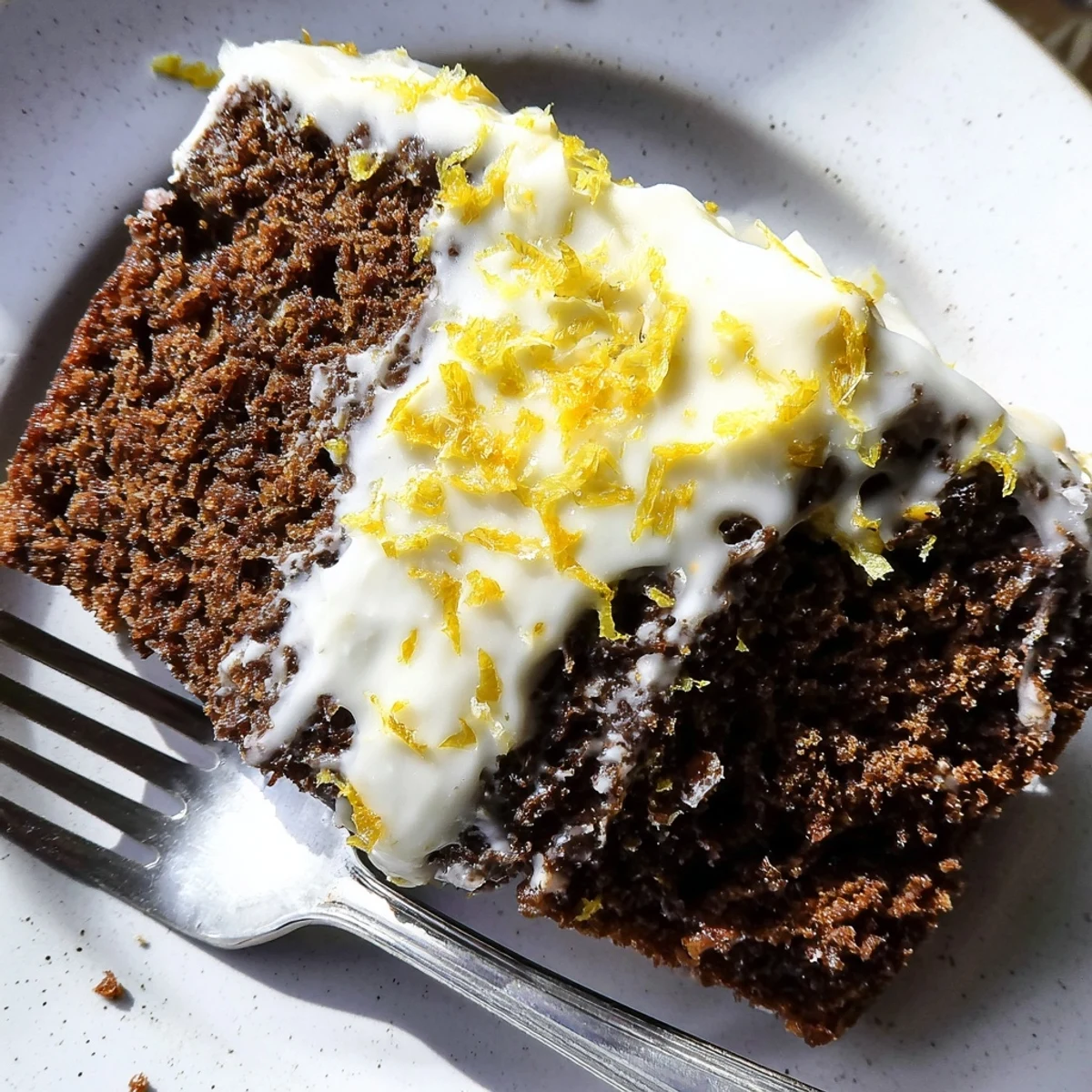 A loaf pan of Gingerbread Loaf with Lemon Cream Cheese Glaze garnished with fresh lemon zest for a festive dessert treat.