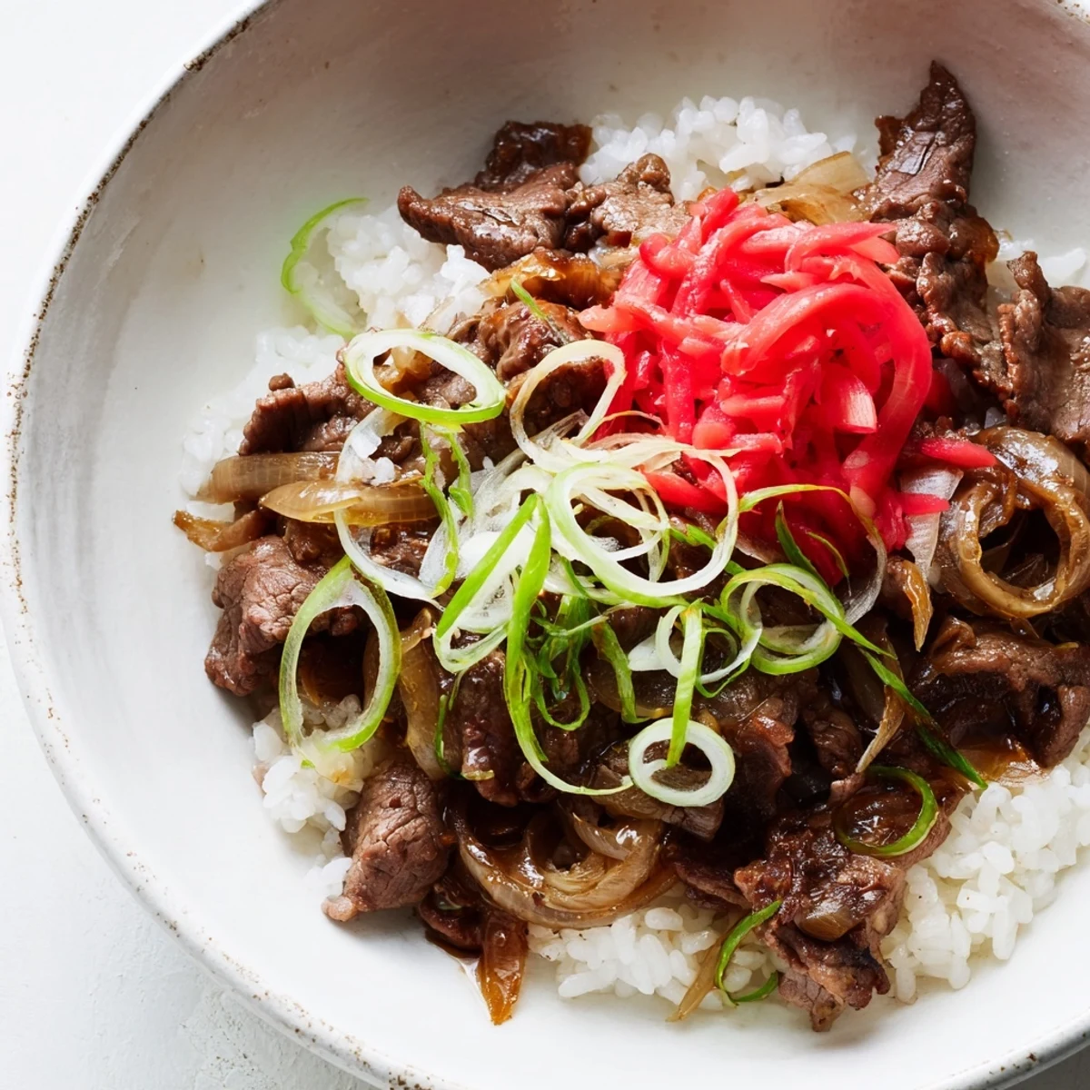 Tender beef and onions simmer in a savory sauce over steamed white rice in this Japanese beef bowl.