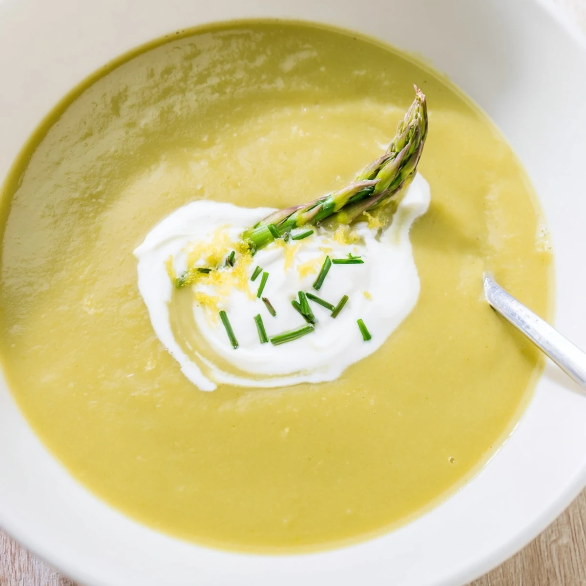A bowl of Creamy Asparagus Soup with Lemon and Crème Fraîche, topped with roasted asparagus tips and lemon zest.