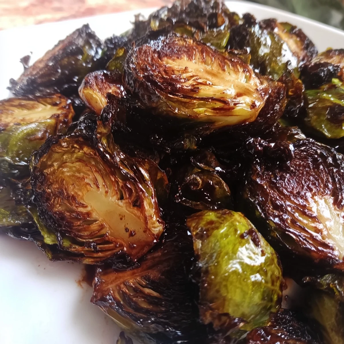 A close-up of crispy caramelized roasted Brussels sprouts with balsamic vinegar drizzle, served warm in a white ceramic bowl.