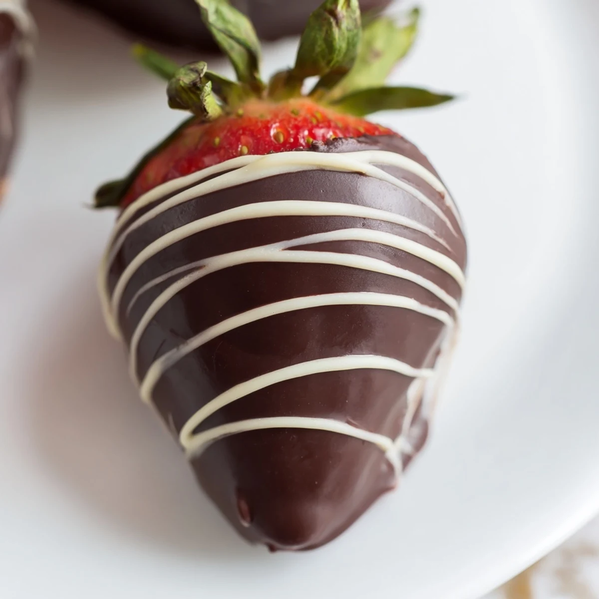 Fresh strawberries with stems fully coated in glossy dark chocolate, drizzled with elegant white chocolate on a parchment-lined tray.