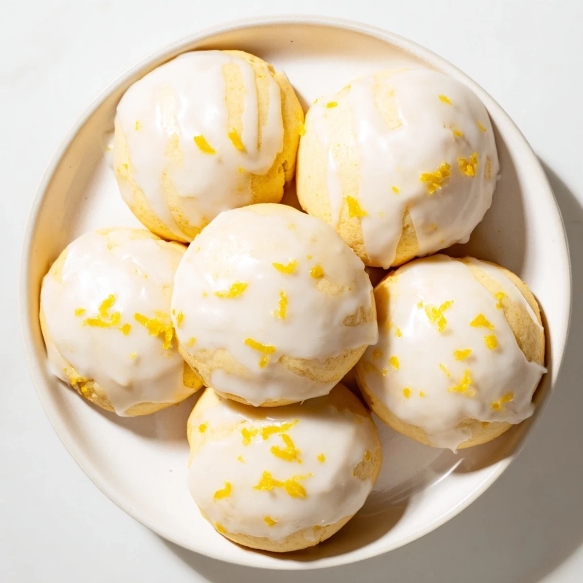 Freshly glazed Lemon Ricotta Cookies arranged on a ceramic plate, ready to serve as an Italian-American dessert, garnished with extra lemon zest.