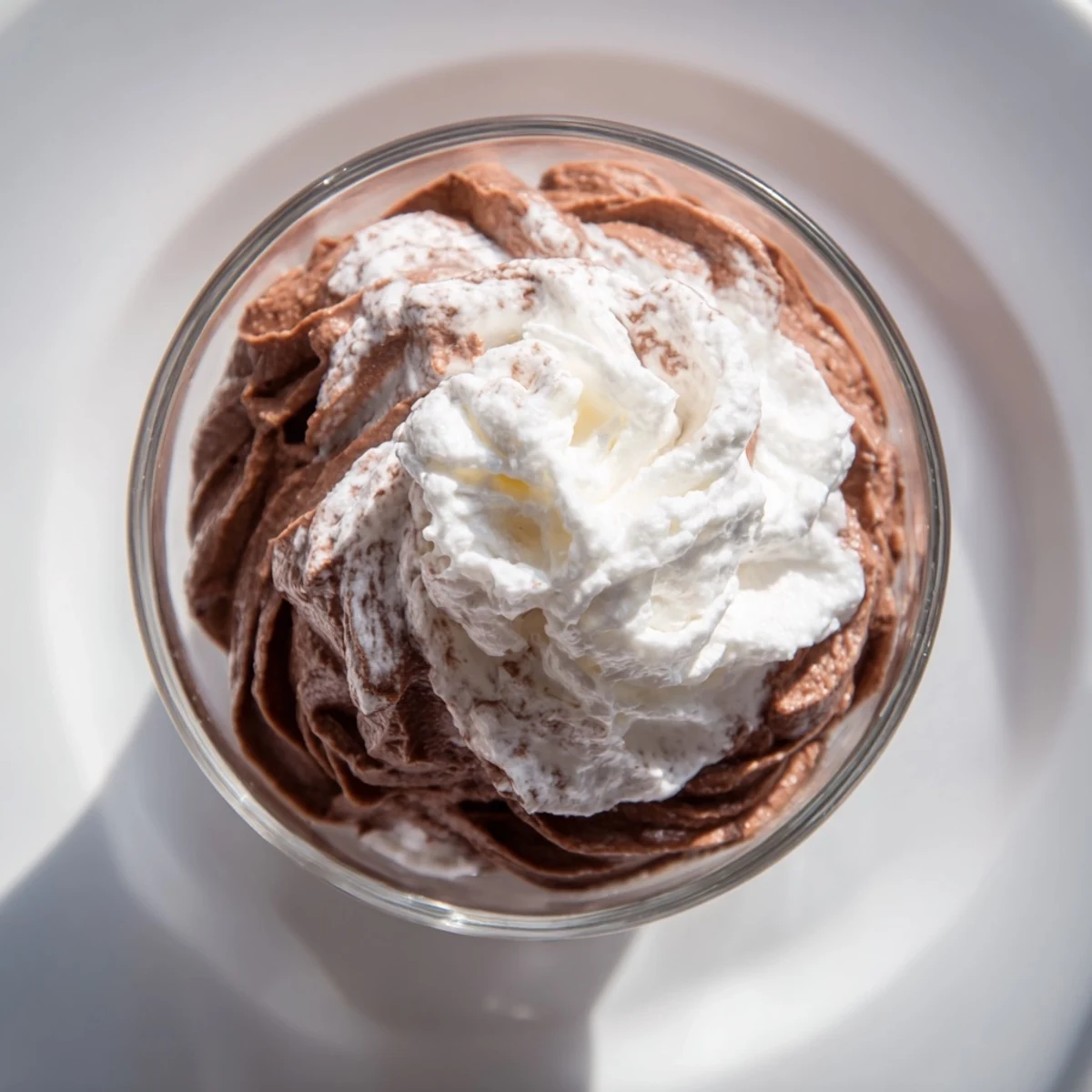 Creamy chocolate mousse topped with soft whipped cream and chocolate shavings in a serving glass.