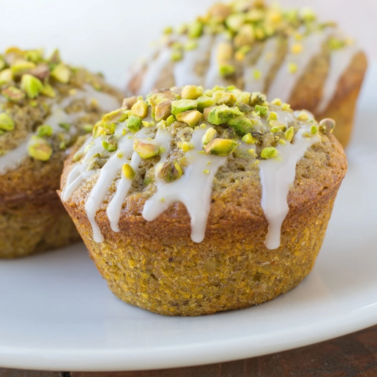 Freshly baked pistachio muffins with vanilla glaze cooling on a wire rack, showcasing moist crumb and chopped nut garnish.  