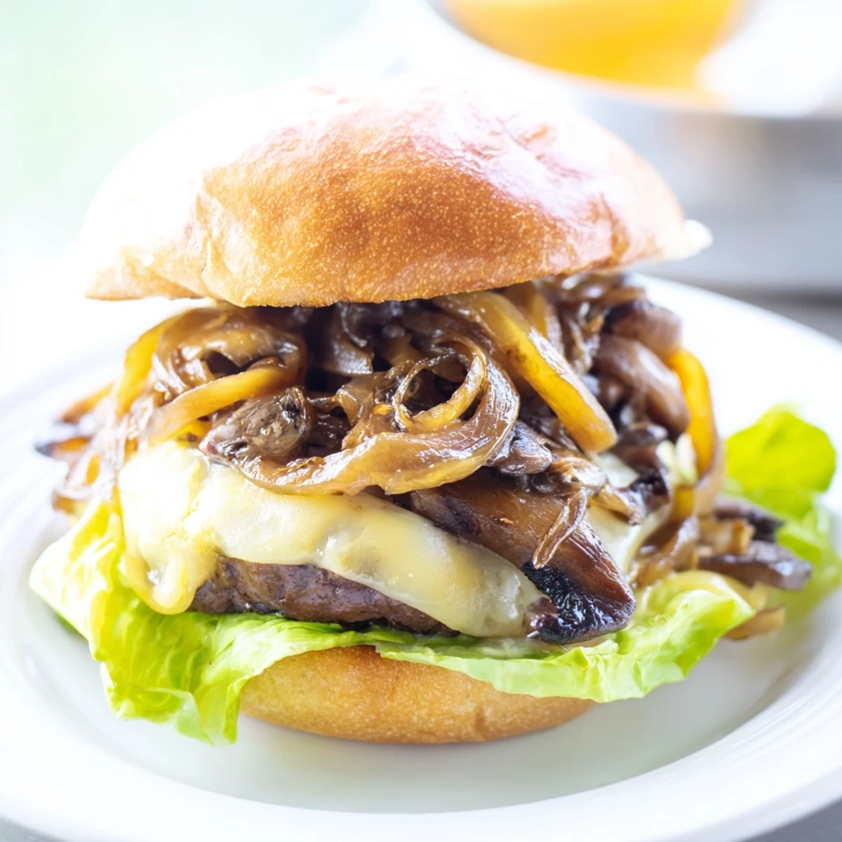The Beef Burger with Caramelized Onions and Mushrooms sits on a white plate beside crispy fries and a dill pickle spear.