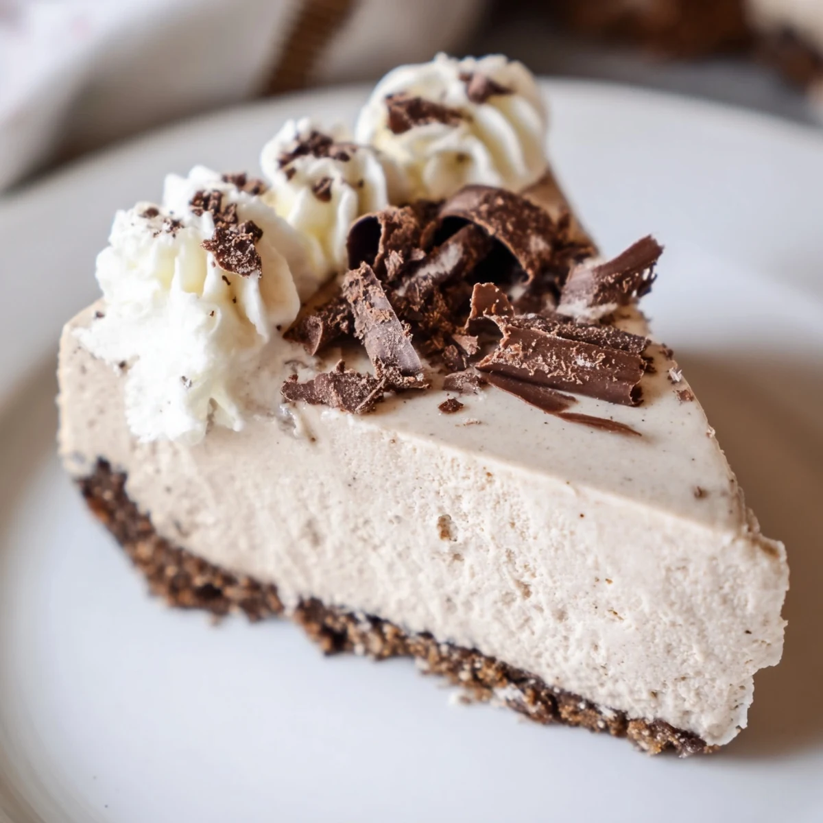 A slice of rich Irish Cream Cheesecake with a smooth creamy filling on a graham cracker crust, served on a dessert plate with chocolate shavings.