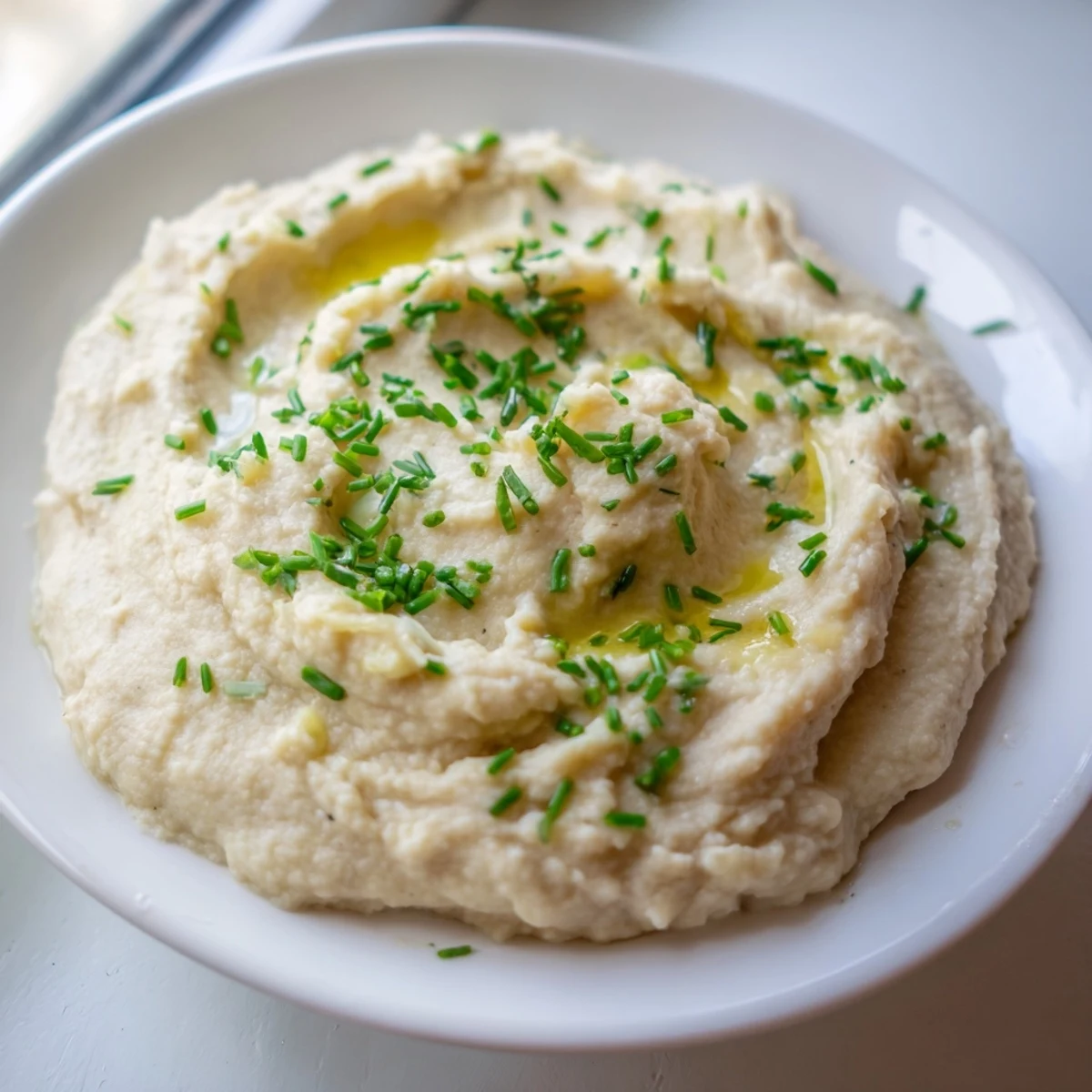 Creamy Roasted Garlic Mashed Cauliflower with Chives garnished with olive oil swirls.