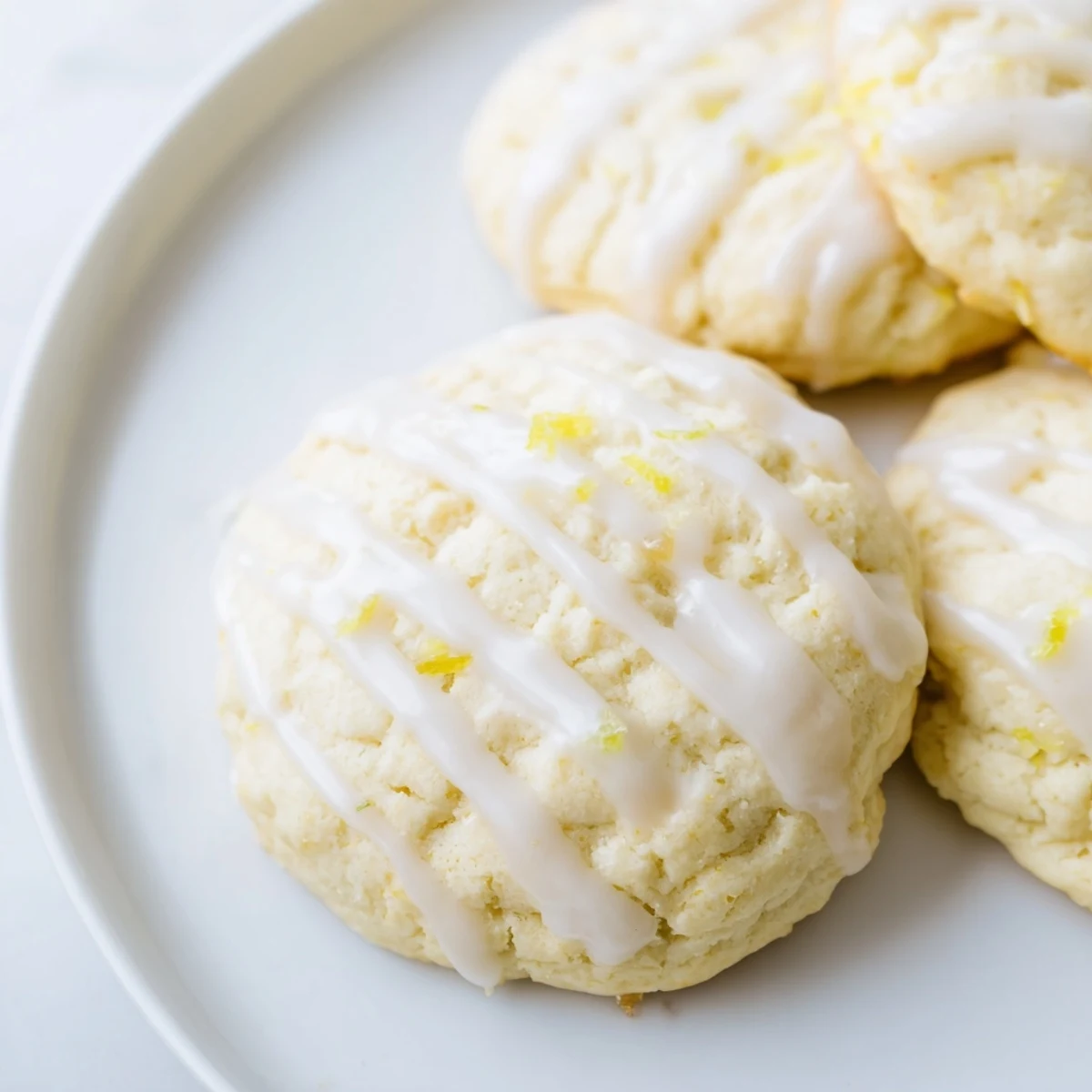 Fresh-baked Lemon Ricotta Cookies sit on a cooling rack with a shiny lemon glaze dripping down the sides.