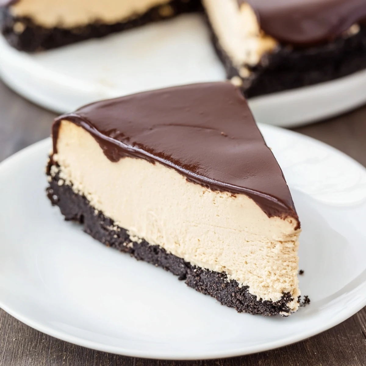 A slice of Irish Cream Cheesecake with Chocolate Ganache on a white plate, showing a creamy filling and glossy dark topping.
