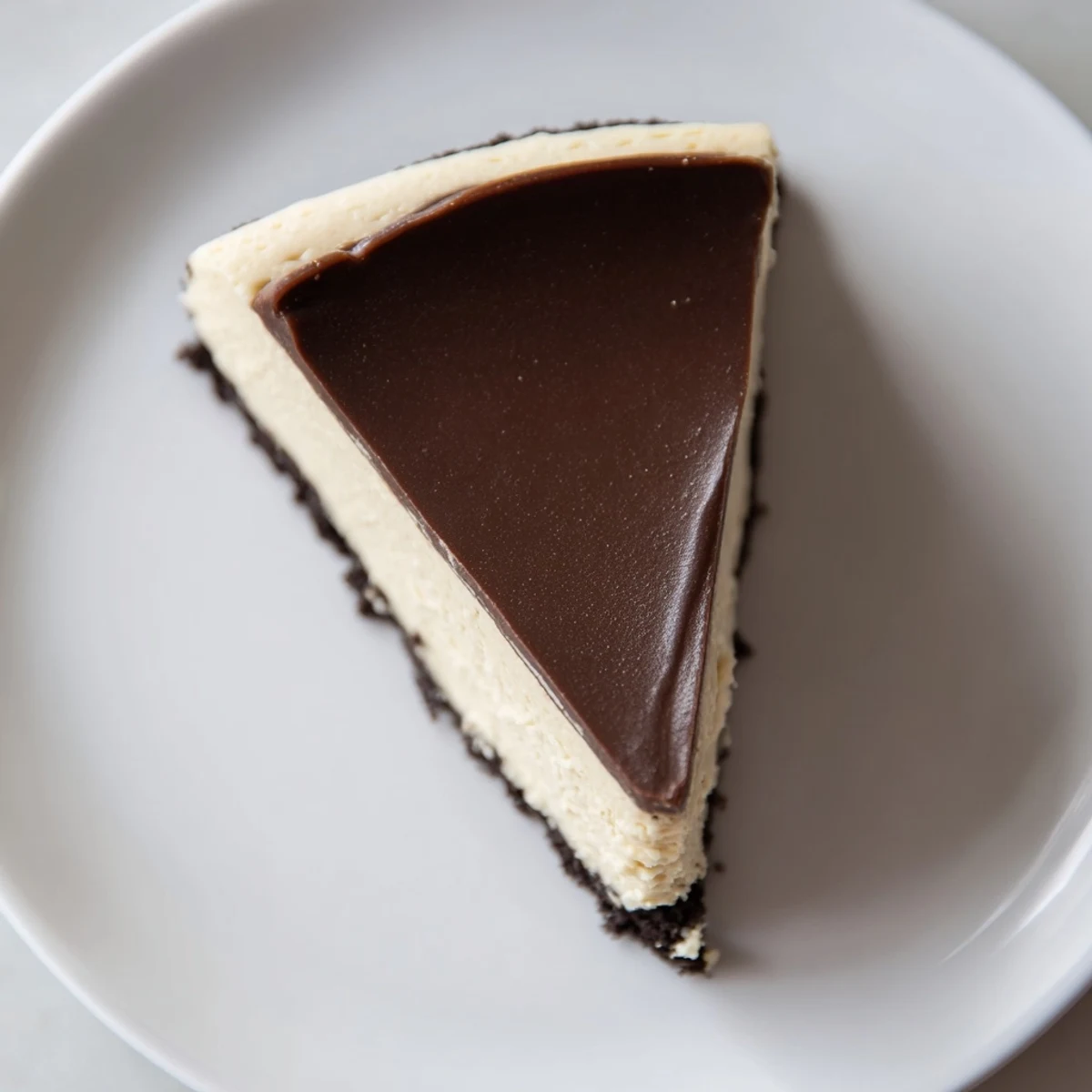 A glossy slice of Irish Cream Cheesecake with Chocolate Ganache shows creamy texture and rich cocoa drizzle on a white plate.