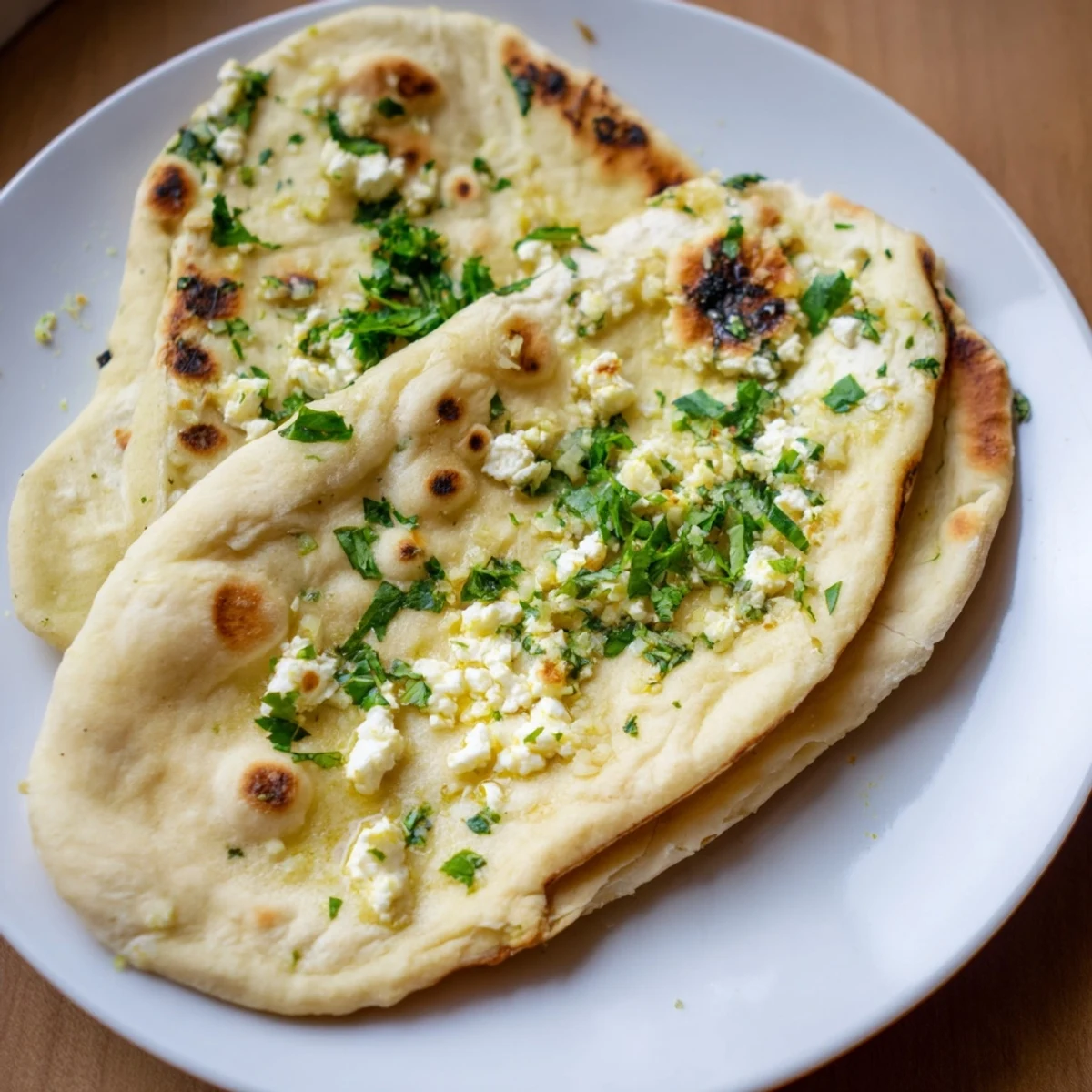 A close-up of golden-brown Cottage Cheese Garlic Naan brushed with melted butter and flecked with fresh cilantro. 