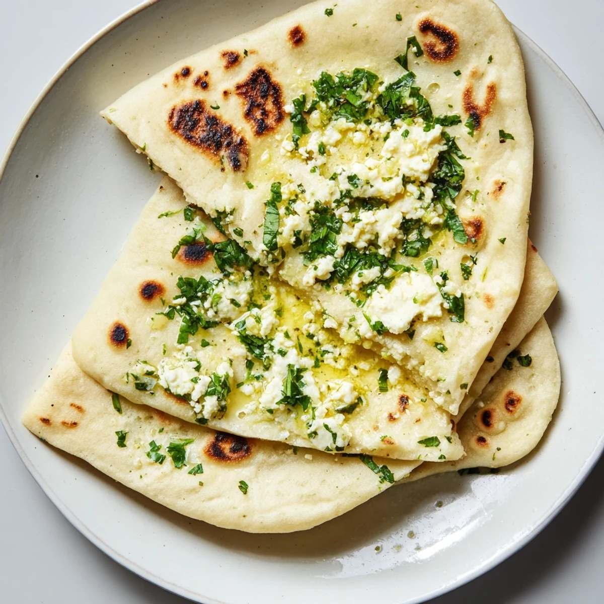 Freshly baked Cottage Cheese Garlic Naan with bubbling cheese peeking from a torn edge, served alongside a bowl of curry. 