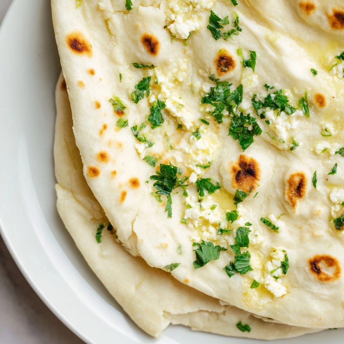 Soft, pillowy Cottage Cheese Garlic Naan stacked on a wooden board, garnished with minced garlic and chopped green chilies.