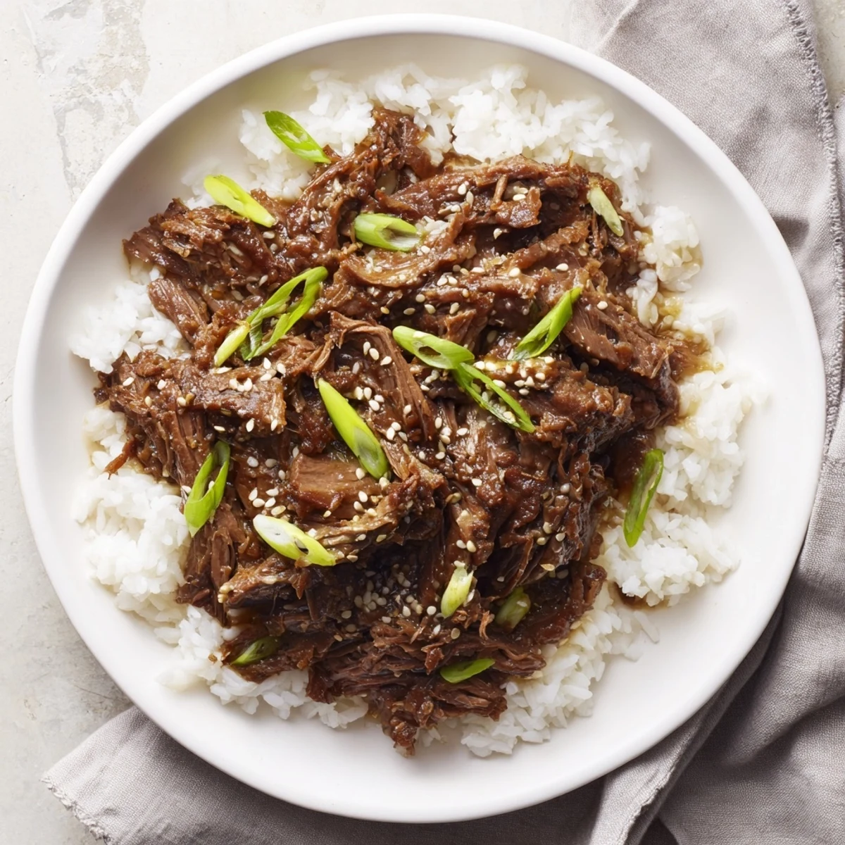 Tender shredded beef from Crock Pot Korean Beef served over steamed rice with green onions and sesame seeds.