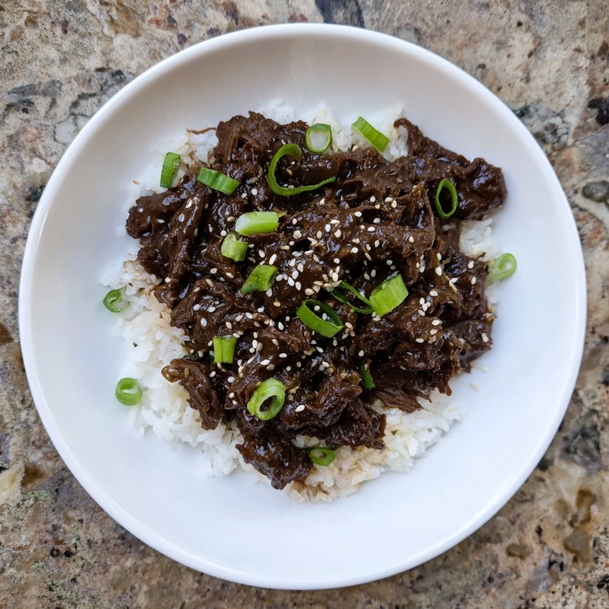 A comforting plate of Crock Pot Korean Beef with slow-cooked beef chunks, rice, and vibrant green onion slices.