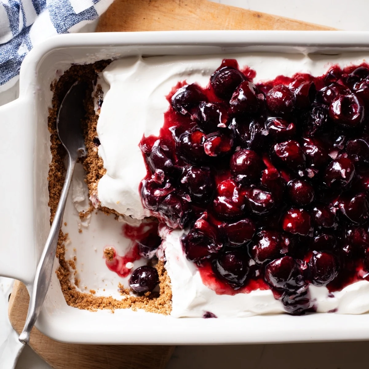 The no-bake Classic Cherry Delight dessert is served in squares on white plates, showcasing its creamy layers and sweet cherry topping. 