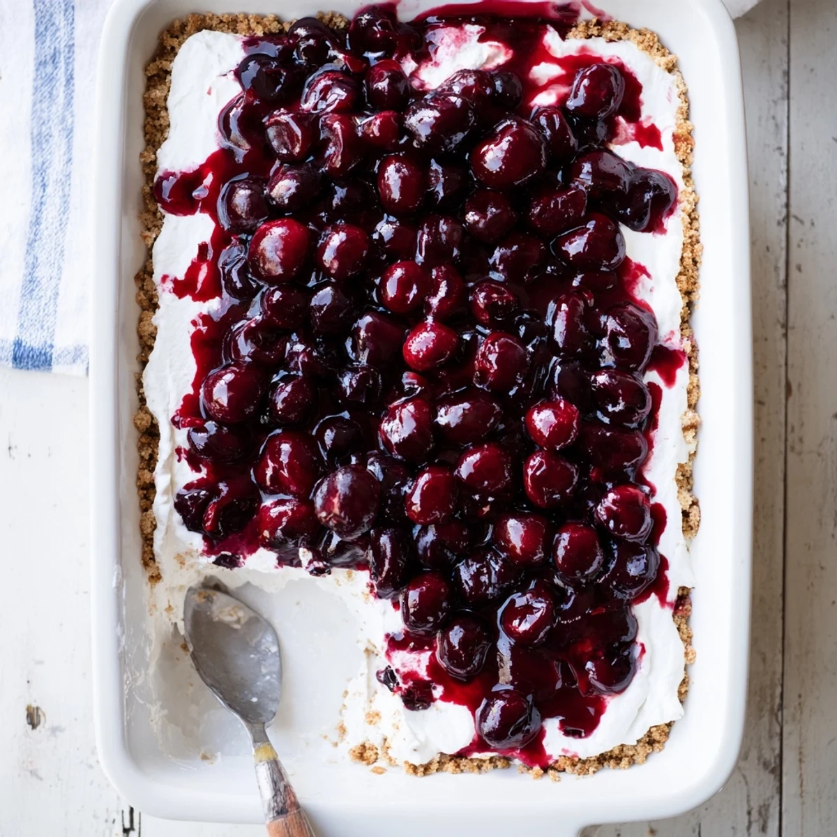 A close-up of Classic Cherry Delight in a glass dish, vibrant red cherries glistening on a creamy white layer above a golden graham cracker crust. 