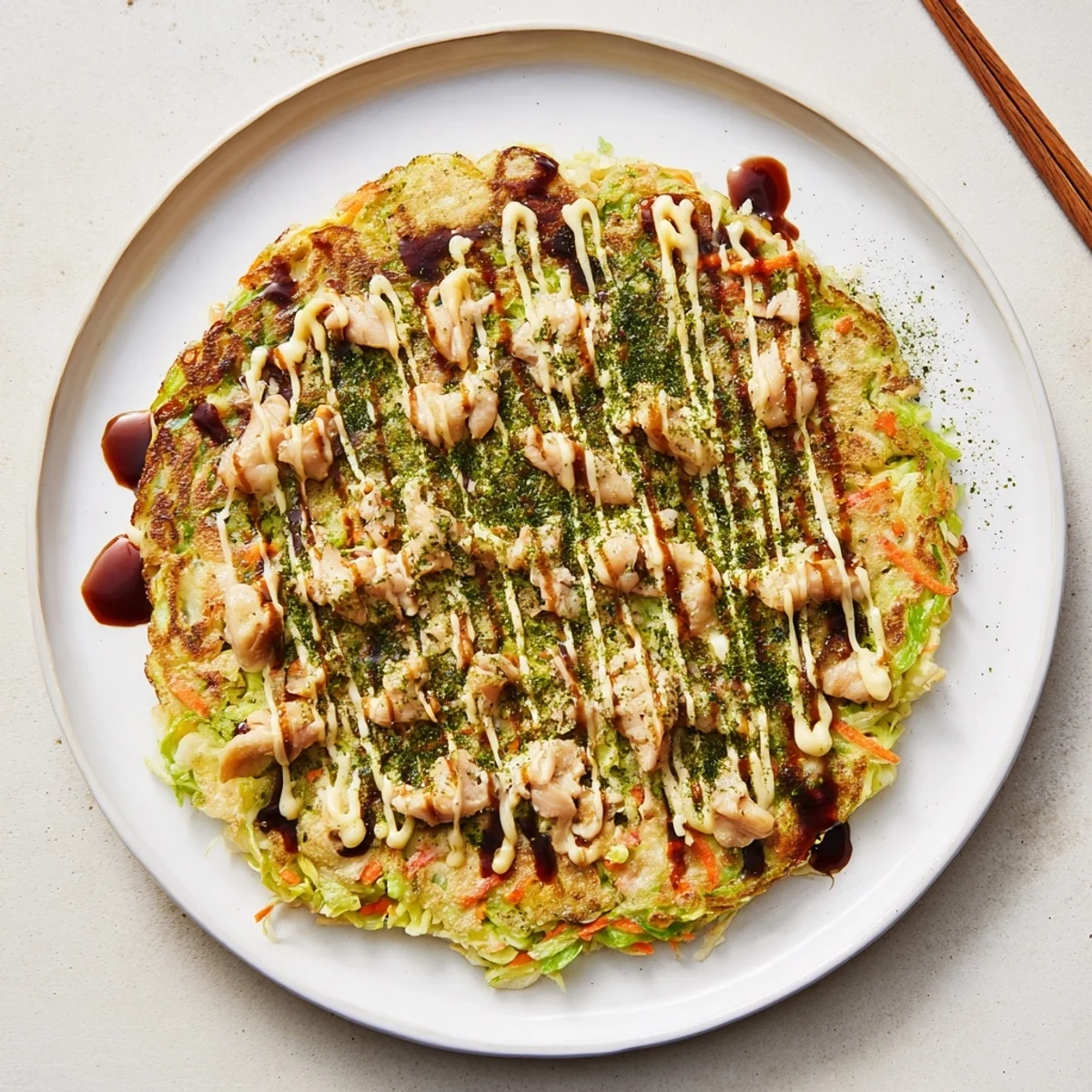 Savory Chicken Okonomiyaki sizzling in a pan, filled with shredded cabbage and tender chicken, ready to be flipped to perfection.
