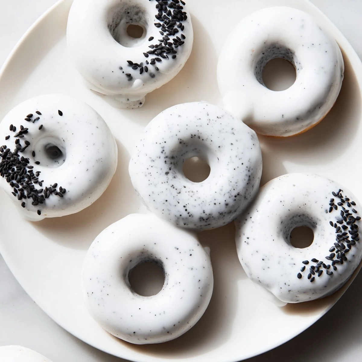 A close-up view of freshly baked Black Sesame Mochi Donuts, glistening with a sweet glaze and sprinkled with extra black sesame seeds.