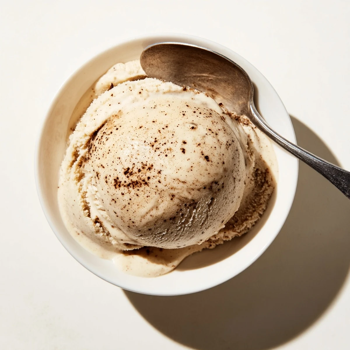 A scoop of Vietnamese Coffee Ice Cream in a chilled glass bowl shows creamy beige swirls flecked with coffee.