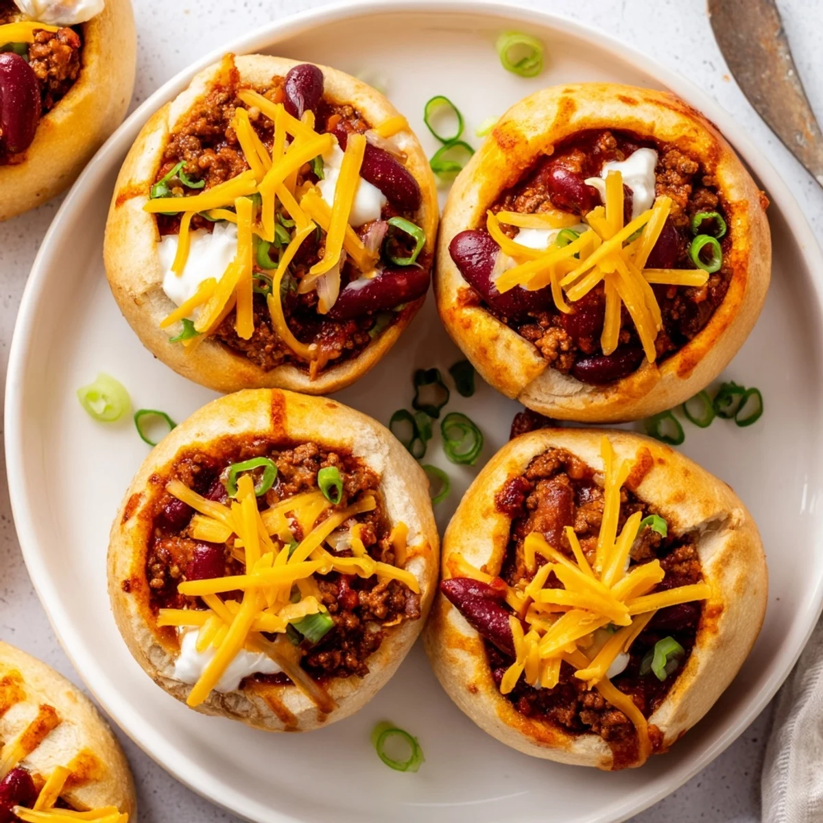 A close-up view shows Mini Chili Football Bread Bowls, the small rolls hollowed out, brimming with rich chili and decorated with white sour cream laces.