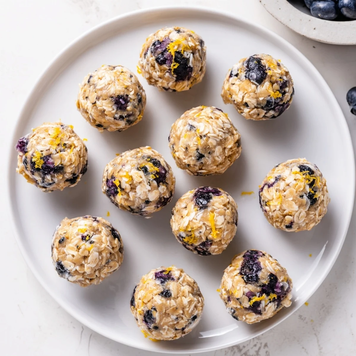 A plated assortment of Blueberry Cheesecake Protein Bites with a few berries scattered nearby, ideal for a gluten-free and high-protein treat.