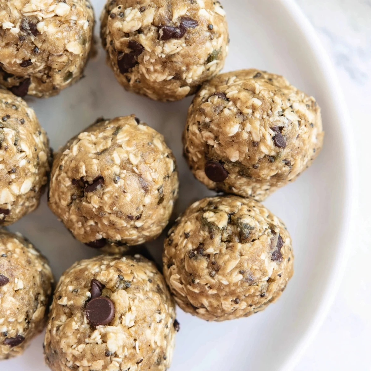 Mint Chocolate Chip Protein Balls are lined up on a white plate, showing their textured oat surface and dark chocolate chips.