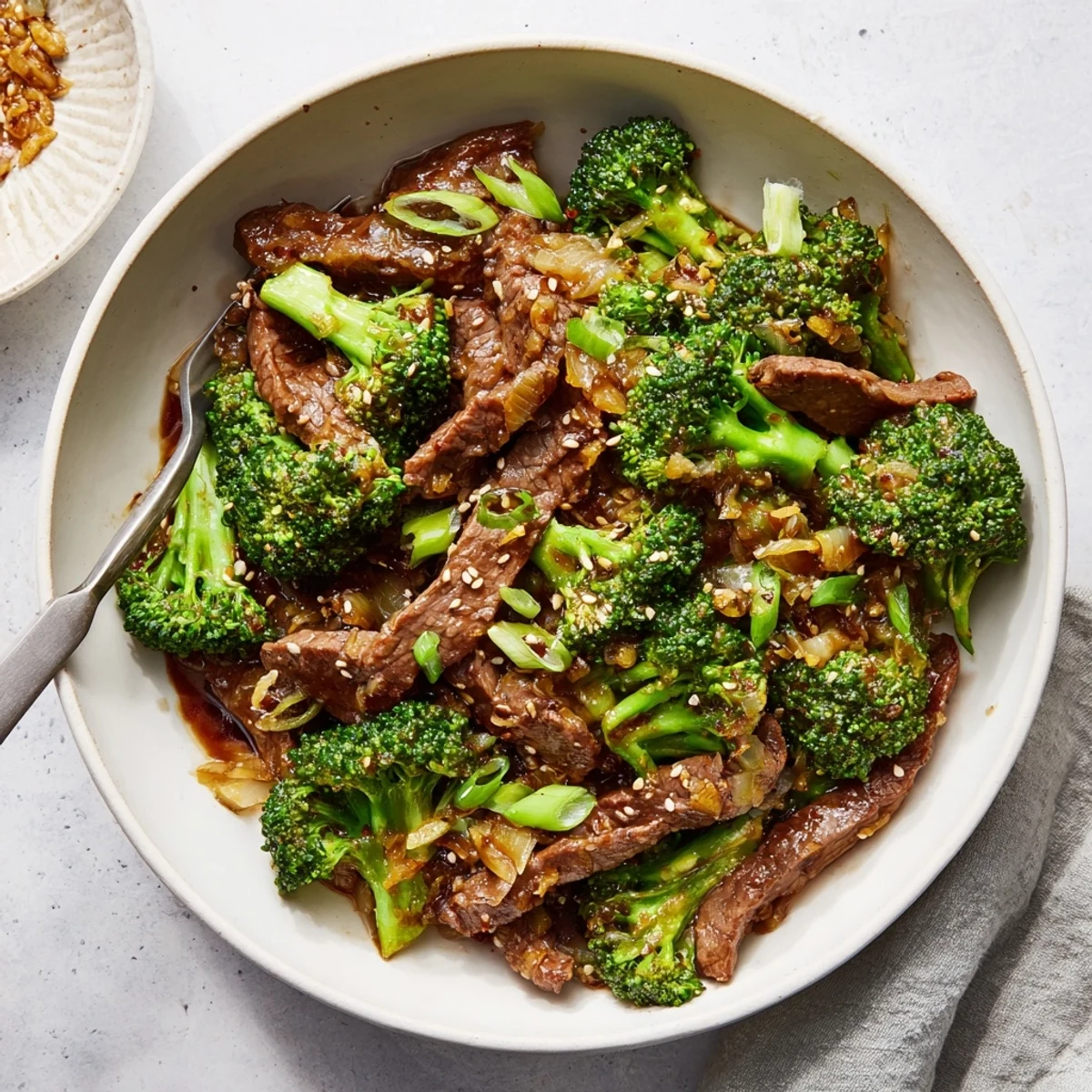 A close-up of Better Than Takeout Beef With Broccoli piled over fluffy white rice, garnished with sesame seeds and fresh green onions.