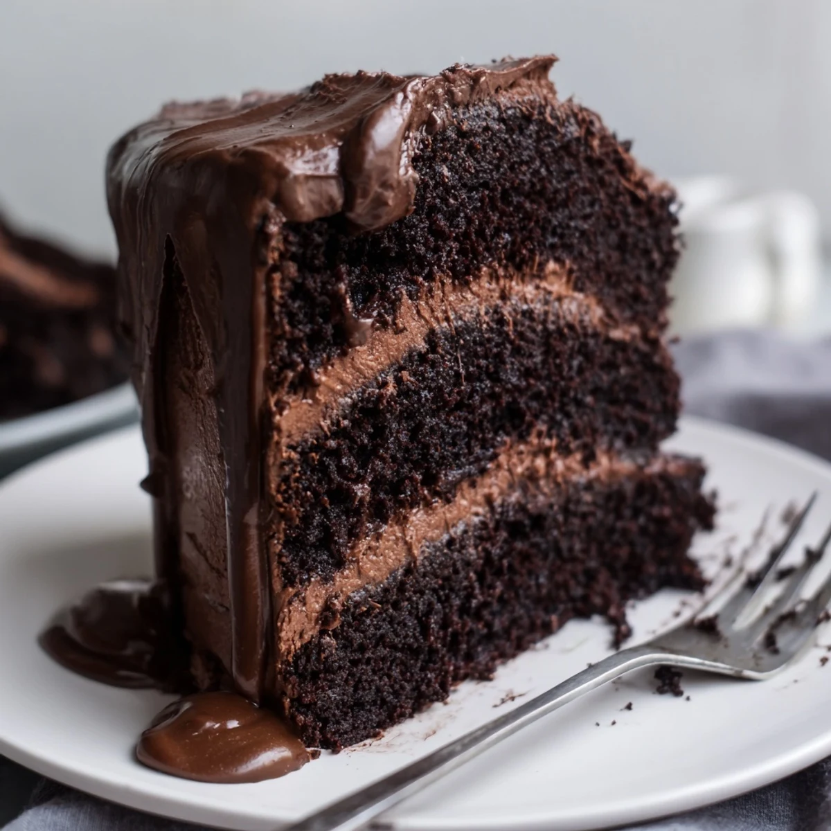 Rich Triple Matilda Chocolate Cake layers with glossy ganache drip on a white plate, served with fresh raspberries for contrast.
