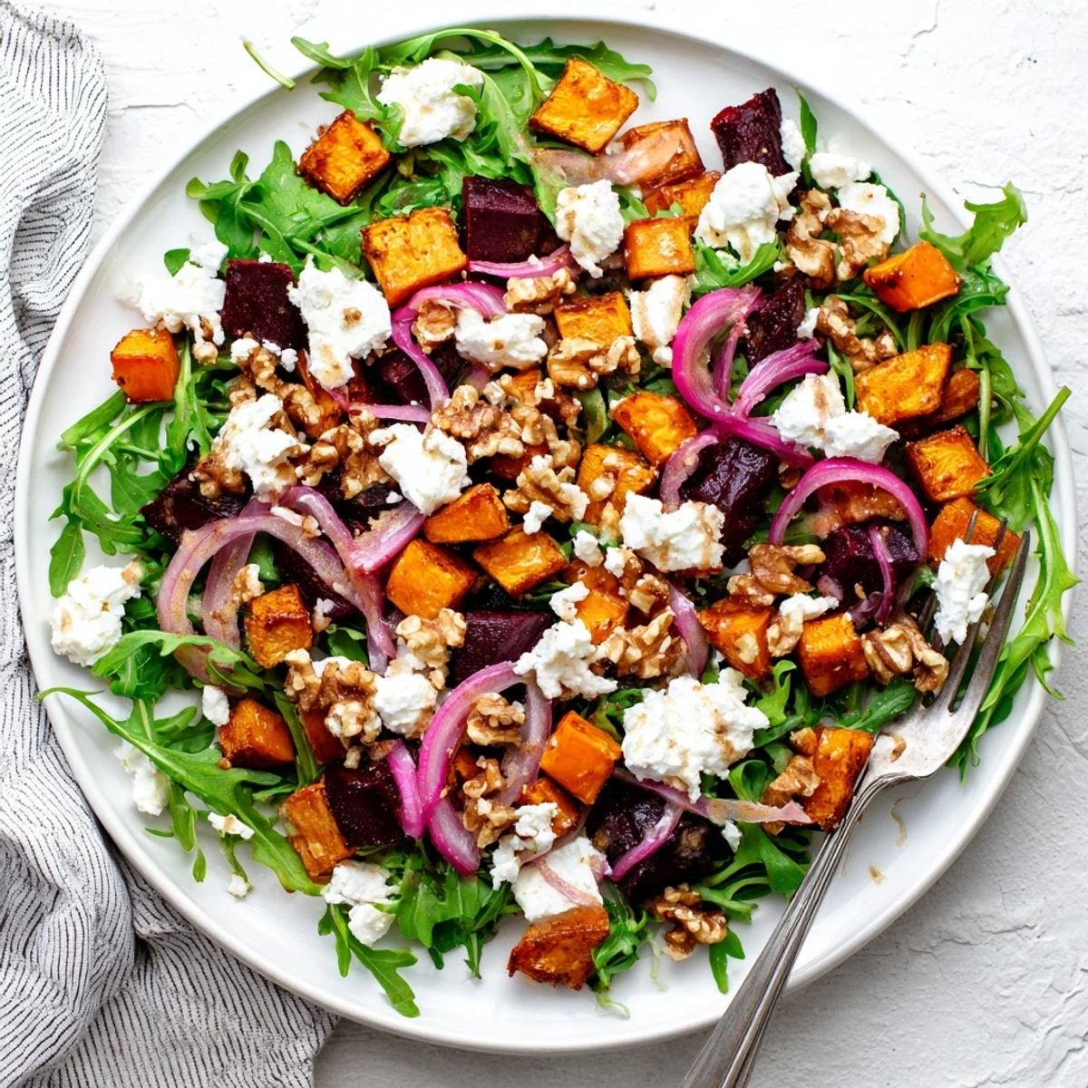 Colorful bowl of creamy roasted beet salad topped with tangy feta and sweet potato chunks