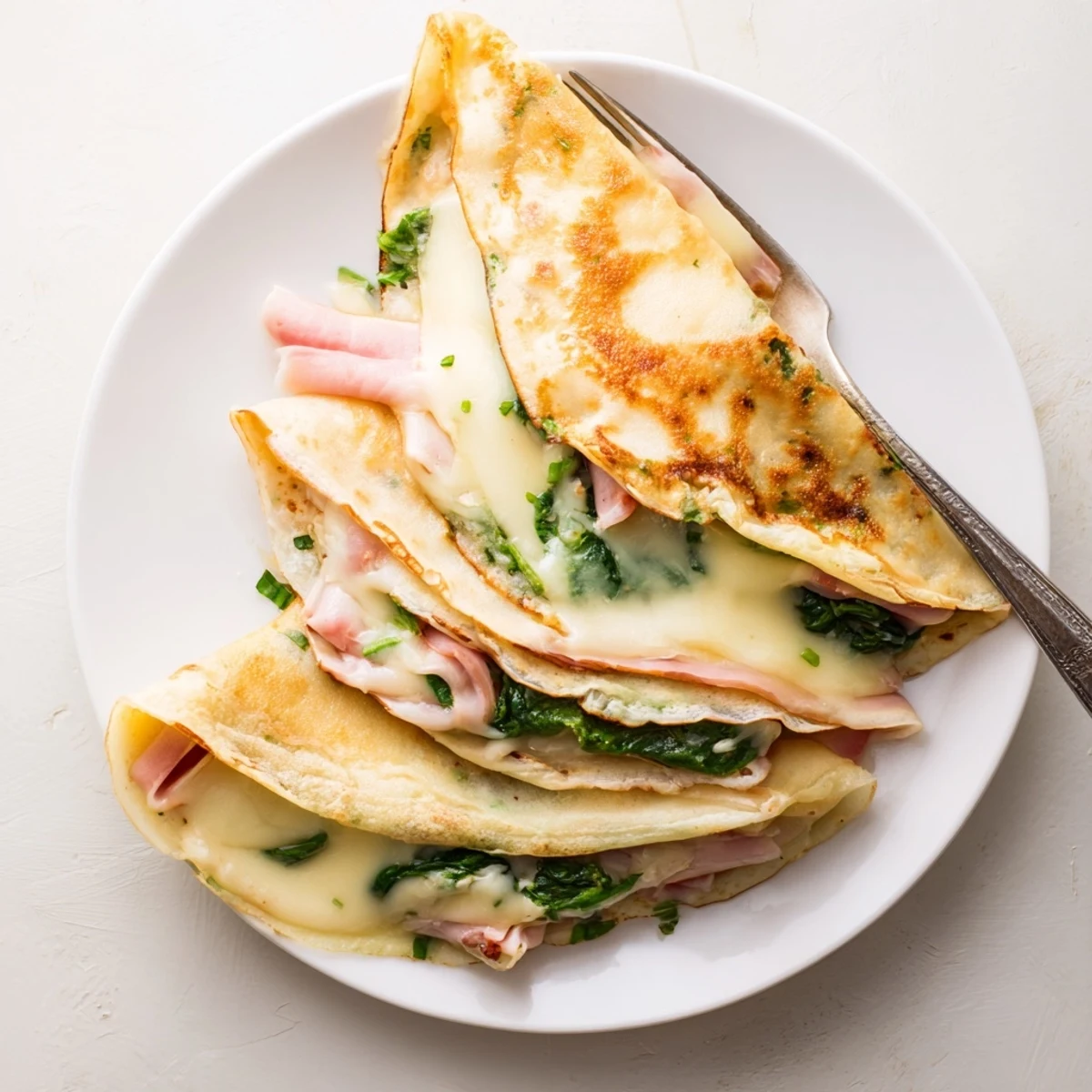 Delicate French savory crepes filled with ham, cheese, and baby spinach baked until bubbly and golden