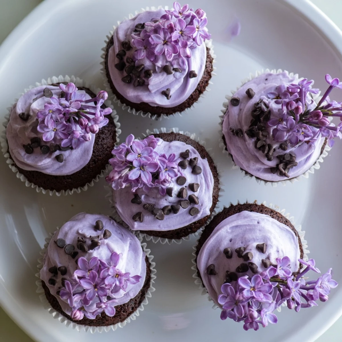 Small batch lilac chocolate cupcakes topped with floral buttercream and fresh purple blossoms on a white plate.