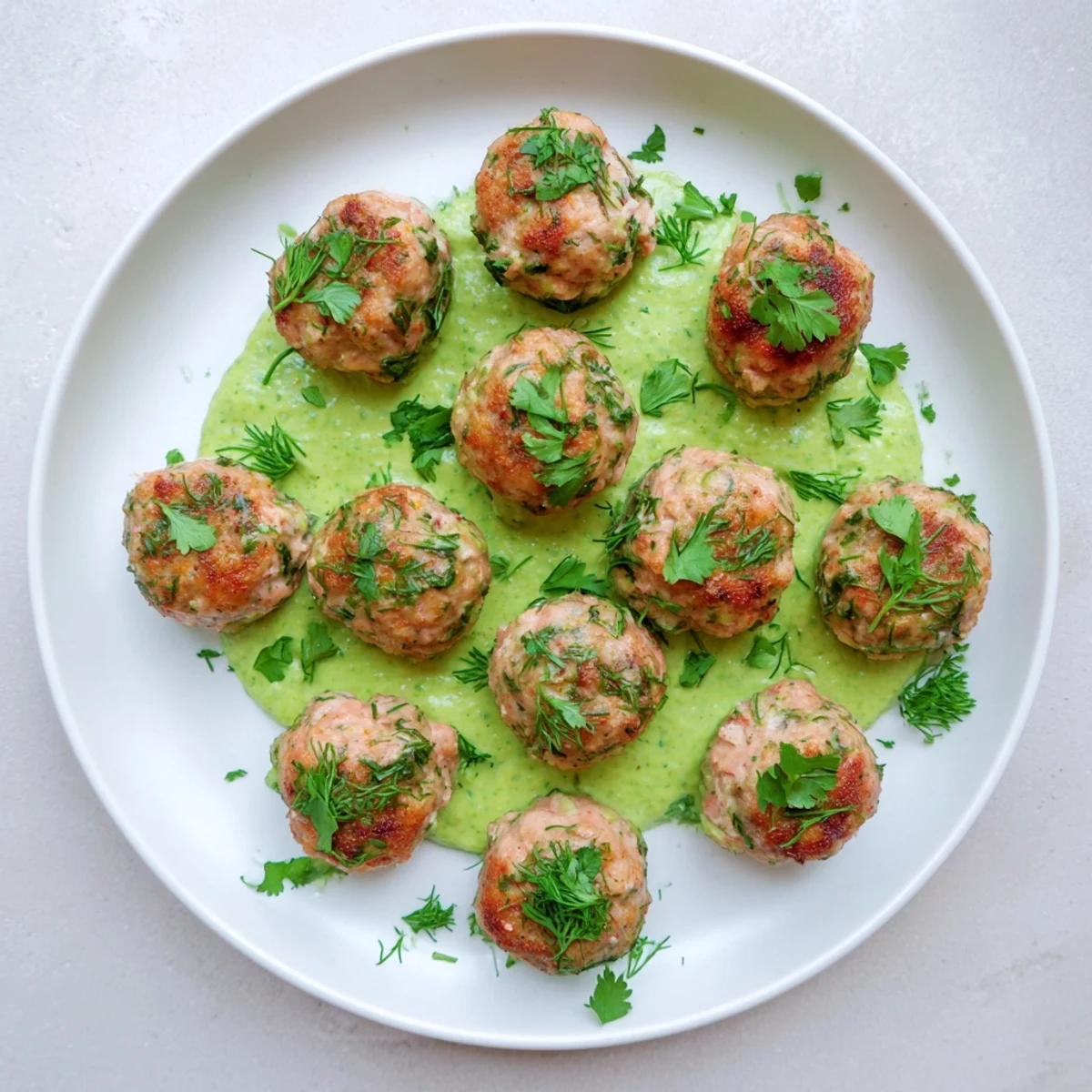 A serving platter of tender baked salmon meatballs paired with zesty avocado sauce for a healthy seafood dinner