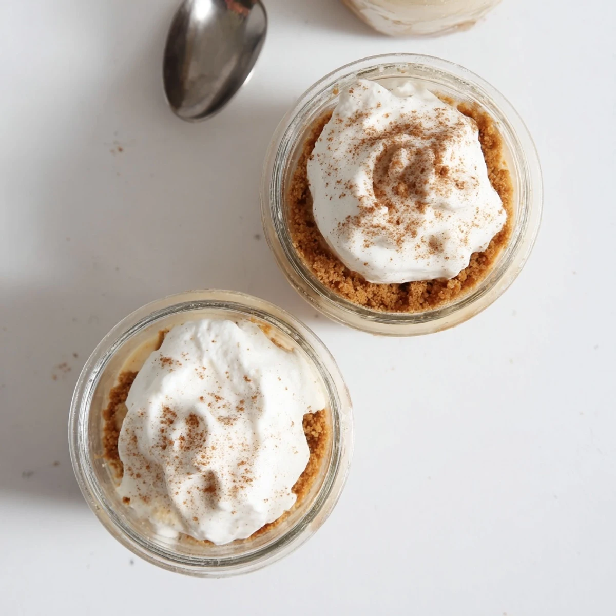 Creamy no bake mini cheesecakes in glass jars showing graham cracker base smooth spiced filling and dusted cinnamon topping