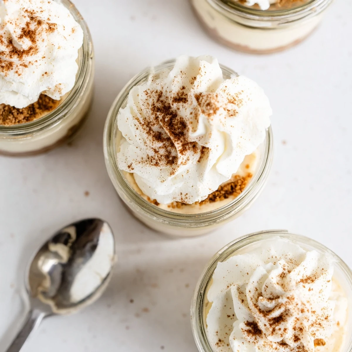 Individual mason jar desserts featuring cinnamon spiced no bake cheesecake with crunchy crust and fluffy white cream topping