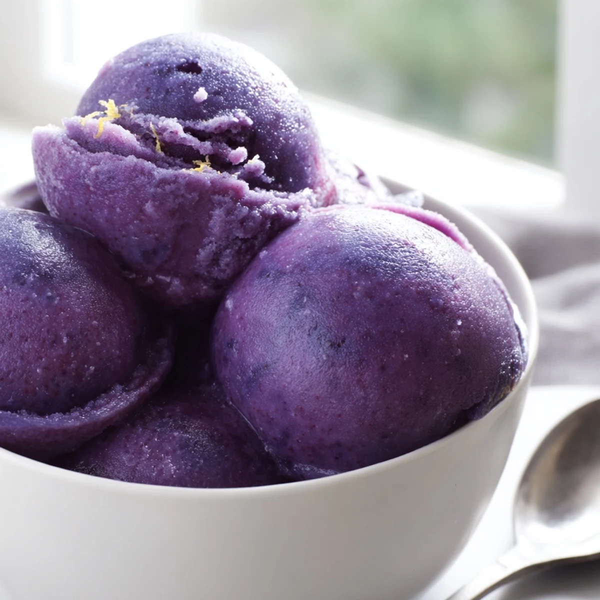 Purple no churn blueberry lemon sorbet scooped into a chilled glass bowl with fresh mint garnish