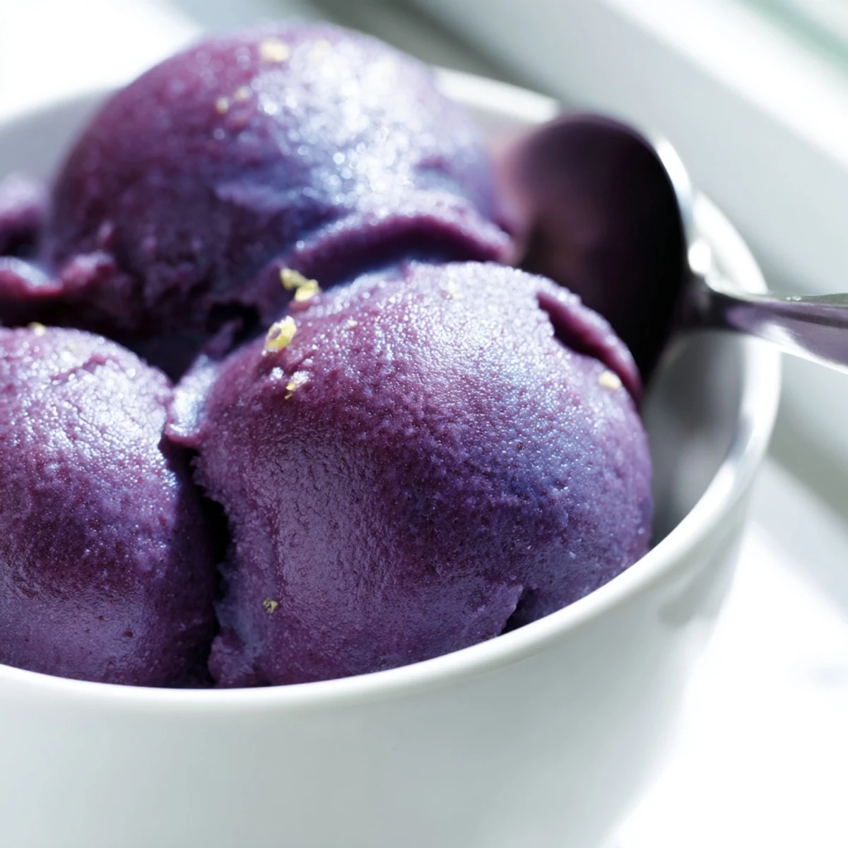 Bright purple no churn blueberry lemon sorbet melting slightly in a white ceramic serving dish