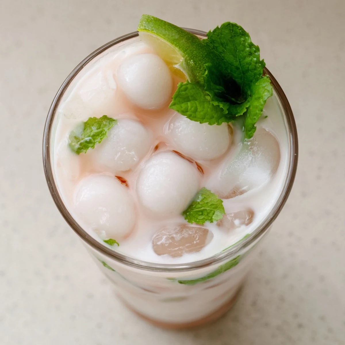 Creamy coconut lychee iced drink topped with fresh mint and lime slices in a tall glass