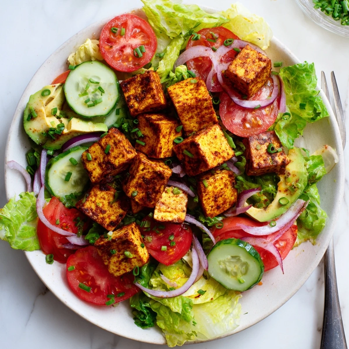 Golden smoky tofu cubes atop crisp romaine lettuce with juicy ripe tomato slices in a summer bowl
