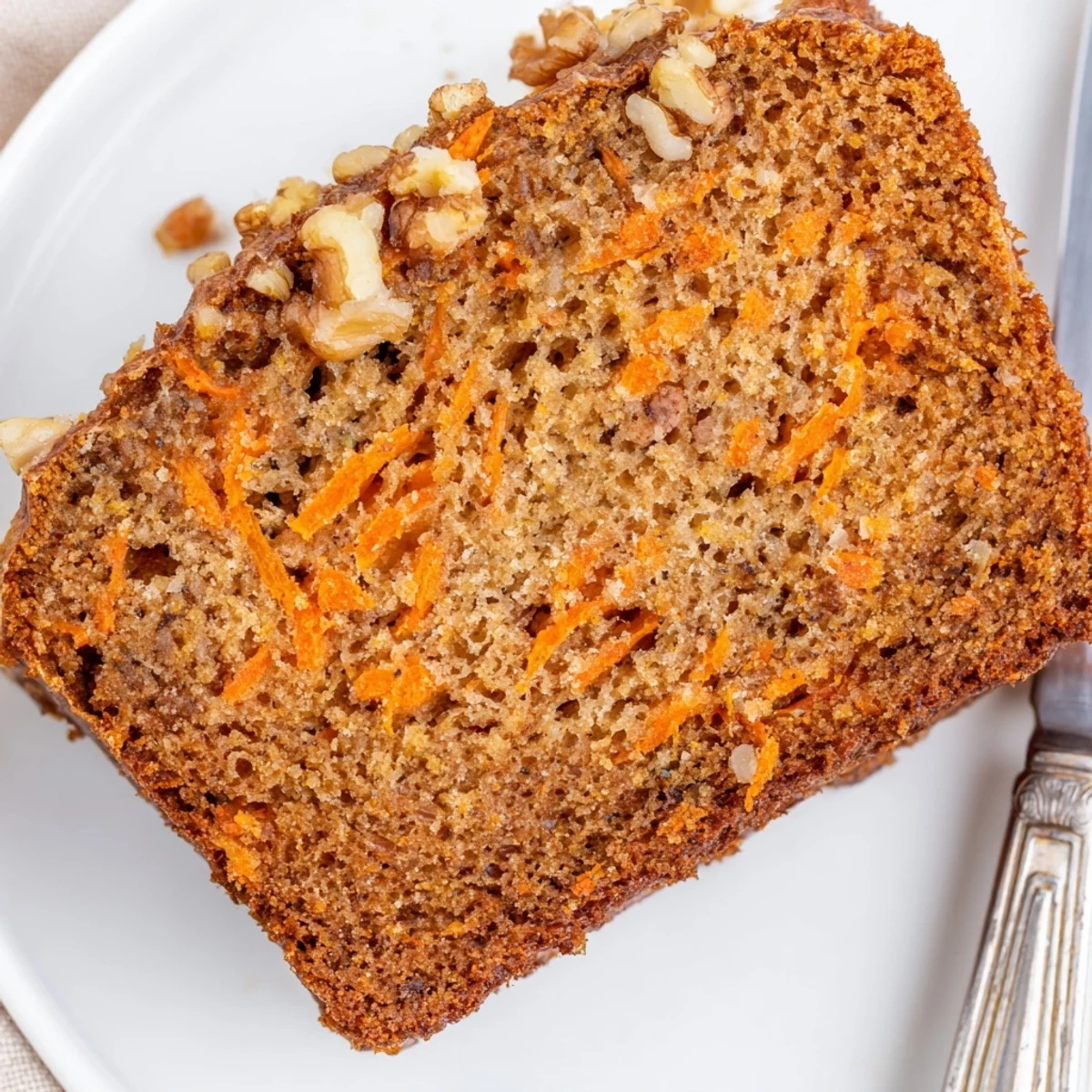 Moist carrot cake banana bread loaf topped with cream cheese frosting and chopped walnuts on a wooden board