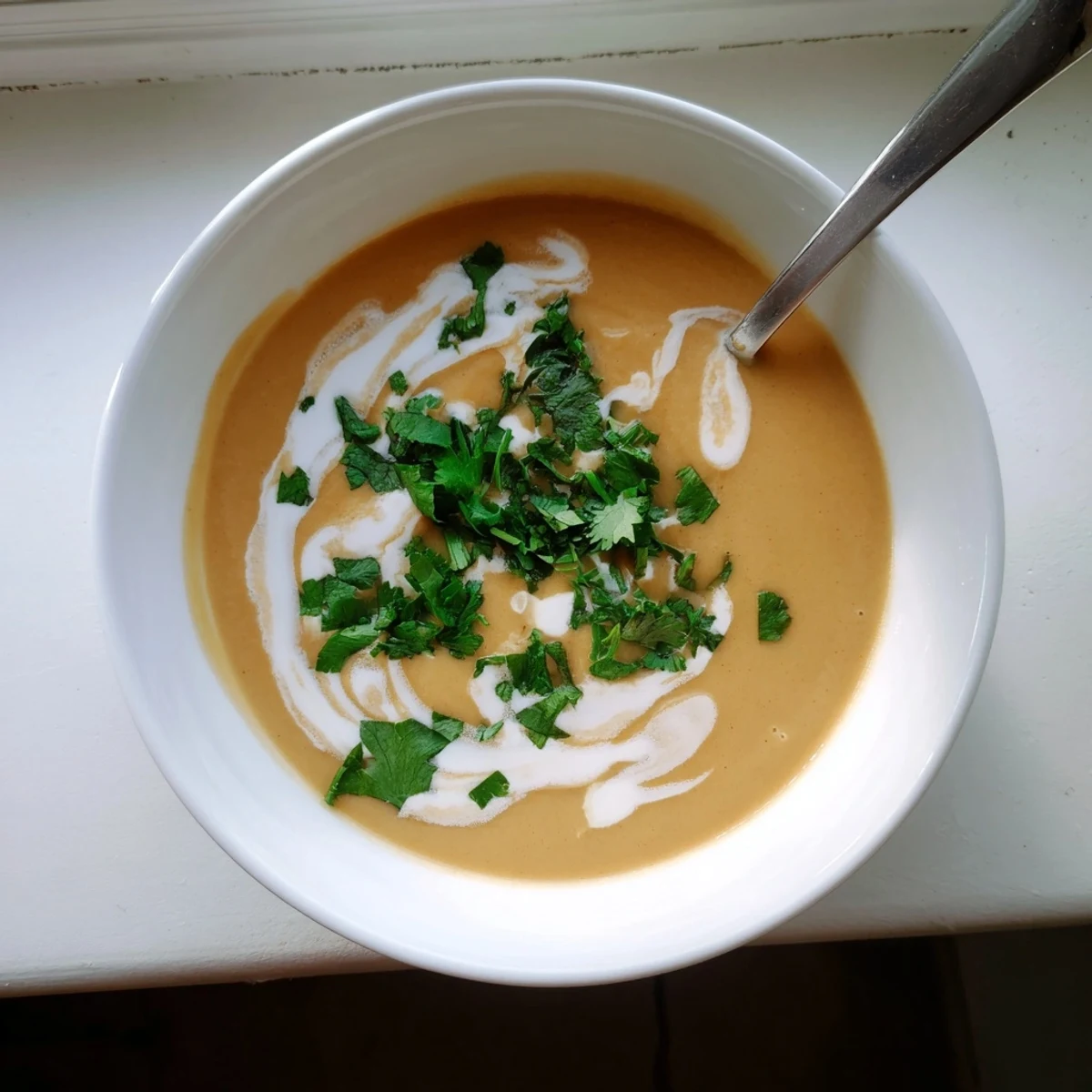 Creamy spicy apple soup garnished with fresh herbs and coconut cream swirl