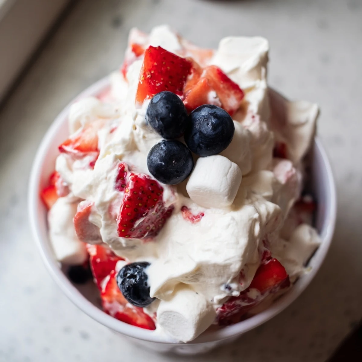 Vibrant strawberries and blueberries folded into fluffy red white blue cheesecake salad
