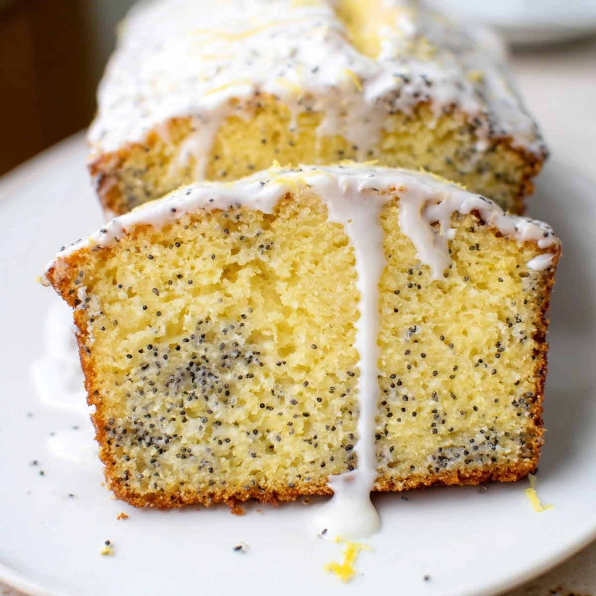 Golden lemon poppy seed loaf cake drizzled with white glaze on a serving plate