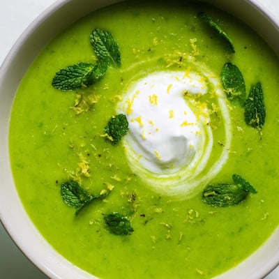A close-up of creamy Spring Pea Soup with Mint and Crème Fraîche, served hot with a golden toast point on the side.