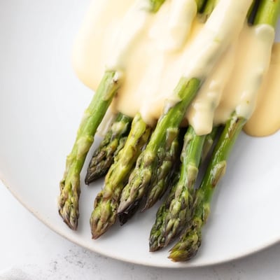 Vibrant roasted asparagus spears piled high, drizzled with creamy, homemade Roasted Asparagus with Hollandaise Sauce for an elegant, classic French side dish.