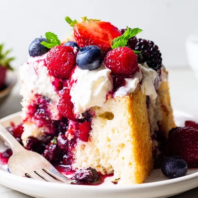 Moist summer berry poke cake dripping with sweet strawberry and blueberry sauce inside.