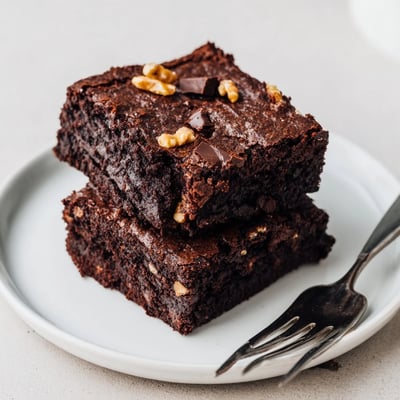 Rich chocolate ultimate brownies topped with scattered walnut pieces on a rustic plate